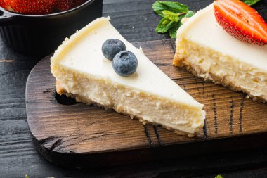 Taze berrie ile ev yapımı cheesecake, siyah ahşap masa arkasında.