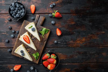 Blueberrie ve çilekli cheesecake, eski koyu ahşap masa arkaplanı, üst görünüm düz metin alanı ile yatıyordu