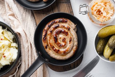 Bavyera usulü kızarmış sosis ve lahana turşusu. Dökme demir tavada, beyaz arka planda, düz manzaralı.