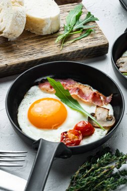 Domuz pastırması ve sebzeli sahanda yumurta, beyaz arka planda dökme demir tavada.