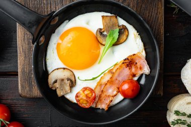 Dökme demir tavada malzemeli sahanda yumurta, eski koyu ahşap masa zemininde, üst manzara düz.