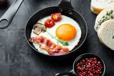 Domuz pastırmalı ve sebzeli sahanda yumurta, siyah arka planda, dökme demir tavada.