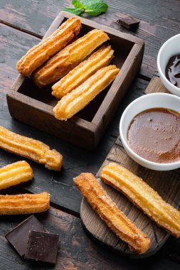 Tipik İspanyol çerez churros, kızarmış hamur pastası genellikle çikolatalı karamelli acı sos setiyle servis edilir, eski, siyah ahşap masa arkasında.