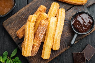 Çikolatalı Churros, geleneksel İspanyol dişi, siyah ahşap masa arkaplanı, üst manzara düz.