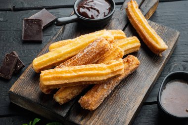Şeker ve çikolata soslu Churros, siyah ahşap masa arkasında.