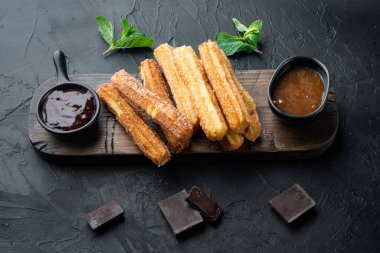 Geleneksel churros çubukları tarçın ve şeker tozu seti, siyah arka planda.