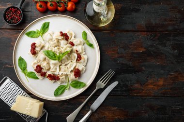 Domates soslu ravioli, peynir ve fesleğen, fesleğen seti, fesleğen, parmesan peyniri ve domates. Eski, siyah ahşap masa arka planında, beyaz tabakta, düz görünüm, metin alanı ve telif alanı.