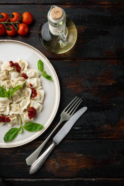 Domates soslu ravioli, peynir ve fesleğen, fesleğen seti, fesleğen, parmesan peyniri ve domates. Eski, siyah ahşap masa arka planında, beyaz tabakta, düz görünüm, metin alanı ve telif alanı.