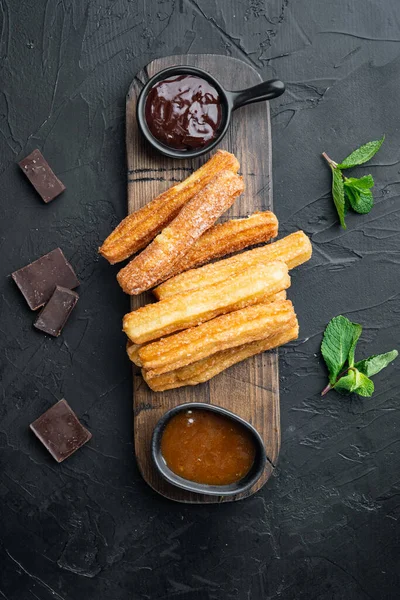 Typical Spanish snack  churros, fried-dough pastry served  usually with chocolate caramel hot sauce set, on black background, top view flat lay