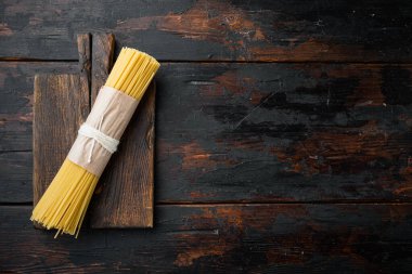 Uzun spagetti. Çiğ spagetti seti, ahşap kesim tahtası, eski koyu ahşap masa arkaplanı, üst görünüm düz, metin alanı ve telif alanı ile