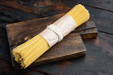 Bir demet spagetti, çiğ İtalyan makarna seti, ahşap kesim tahtası, eski siyah ahşap masa arkaplanı