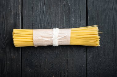 Kurutulmuş spagetti makarna, siyah ahşap masa arkaplanı, en üstteki düz görünüm.