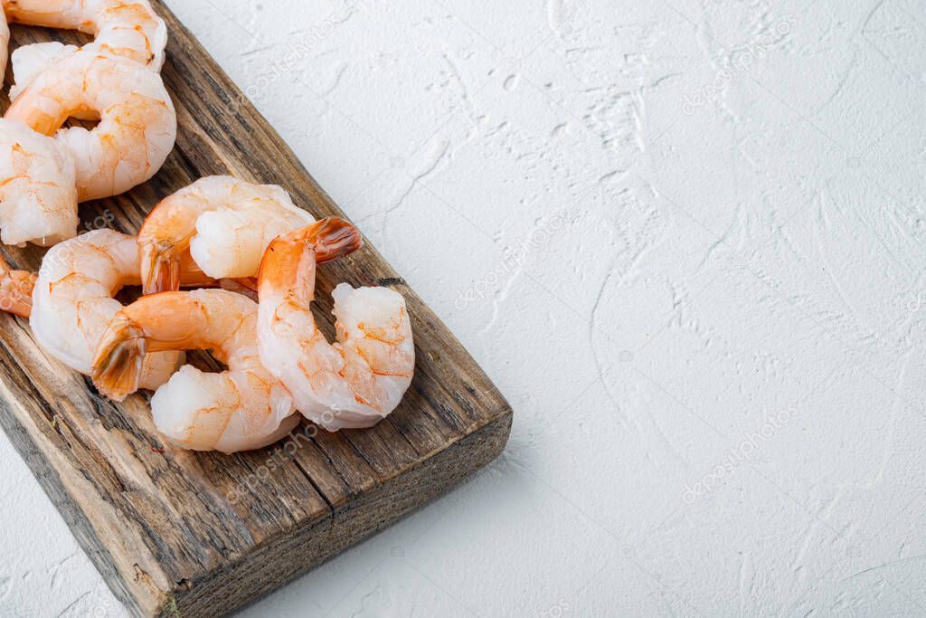 Fresh raw peeled king prawn shrimps with tail set, on wooden cutting board, on white background , with copyspace  and space for text