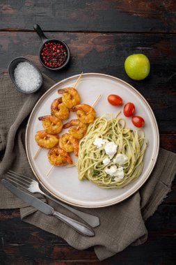 Pesto soslu yeşil spagetti ve ızgara karides şiş seti, tabakta, eski siyah ahşap masa zemininde, üst düz manzaralı