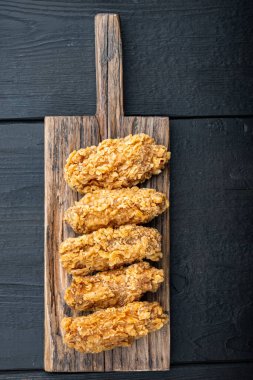 Kızarmış tavuk kanadı parçaları siyah ahşap masa üzerinde, üst manzara.