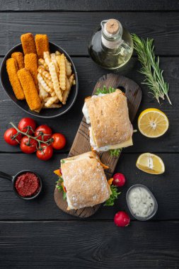 Kırılmış balık setiyle ev yapımı baget, ahşap kesim tahtasının üzerinde, siyah ahşap masa zemininde, üst manzara düz yatıyordu.