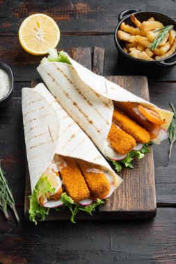 Balık kroketli tortilla rulosu, peynir ve sebze seti, ahşap kesme tahtasının üzerinde, eski siyah ahşap masa arkasında