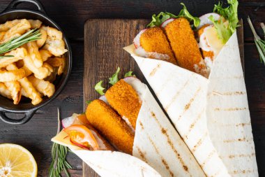 Balıklı sandviç rulosu, peynir ve sebze seti, ahşap kesim tahtası, eski siyah ahşap masa arka planı, üst görünüm düz