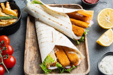 Balık kroket, peynir ve sebzeli tortilla sarması, ahşap tepside, gri arka planda.