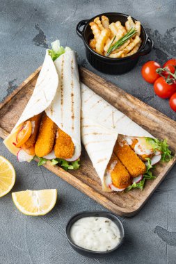 Balık kroket, peynir ve sebzeli tortilla sarması, ahşap tepside, gri arka planda.