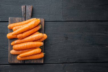 Taze ve tatlı havuç demeti, ahşap kesim tahtasında, siyah ahşap masa zemininde, telif alanı ve metin için yeri olan üst manzara düzlüğü