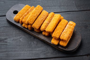 Donmuş balık çubukları seti, tahta kesme tahtası, siyah ahşap masa arkaplanı.