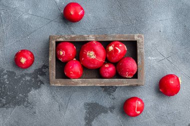 Sebze yığını, kırmızı turpların etrafında, tahta kutuda, gri arka planda, üst manzara düz yatıyordu.