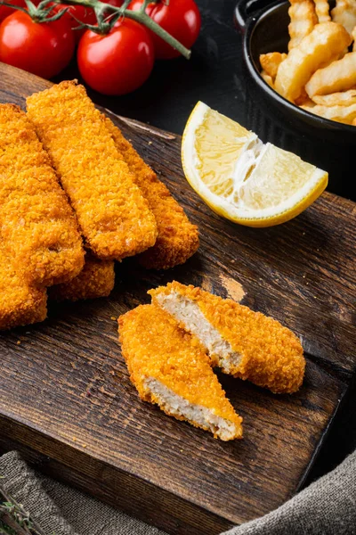 Fried fish finger stick or french fries fish with sauce set, on wooden cutting board, on black background