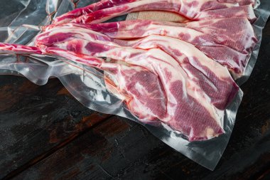 Plastik vakum paketinde kuzu pirzolası pişirmek için kuzu kaburgaları, eski koyu ahşap masa arka planında, metin alanı ve yeri ile