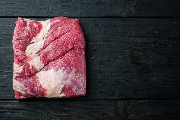 Raw piece of marble beef brisket set, on black wooden table background, top view flat lay,  with copy space for text
