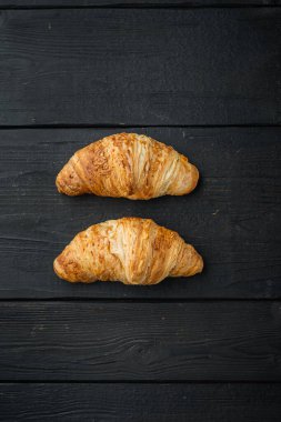 Taze pişmiş kruvasan seti, siyah ahşap masa zemininde, üst manzara düz.