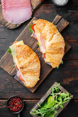 Kruvasan sandviç seti, bitkiler ve malzemelerle, eski siyah ahşap masa arka planında, üst manzara düz yatıyordu