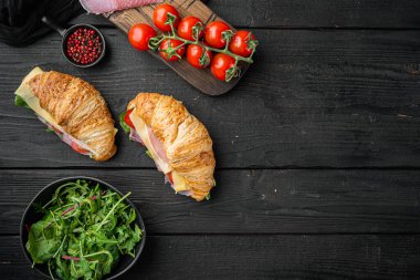 Prosciutto, domates, peynir seti, otlar ve malzemelerle kaplı kruvasan sandviçi, siyah ahşap masa arkaplanı, üst görünüm düz, metin alanı için kopya alanı