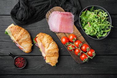 Kruvasan sandviç seti, otlar ve malzemelerle, siyah ahşap masa zemininde, üst manzara düz.