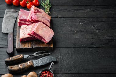 Çiğ sığır eti kısa kaburga seti, malzemeleri ile, ve eski kasap satır bıçağı, siyah ahşap masa arka planı üzerinde, metin için kopyalama alanı ile