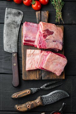 Çiğ Organik Biftek Kaburgaları Pişirmeye Hazır, malzemeleri ile, ve eski kasap satır bıçağı, siyah ahşap masa arka planı, üst görünüm düz yatıyordu