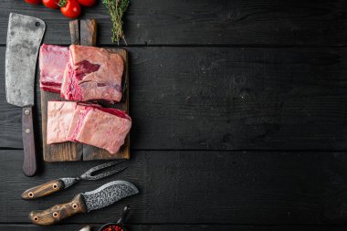 Çiğ Kara Angus Mermer Kaburga seti, malzemeleri ve eski kasap satırı bıçağı, siyah ahşap masa arka planı, üst görünüm düz, metin alanı için kopya alanı ile