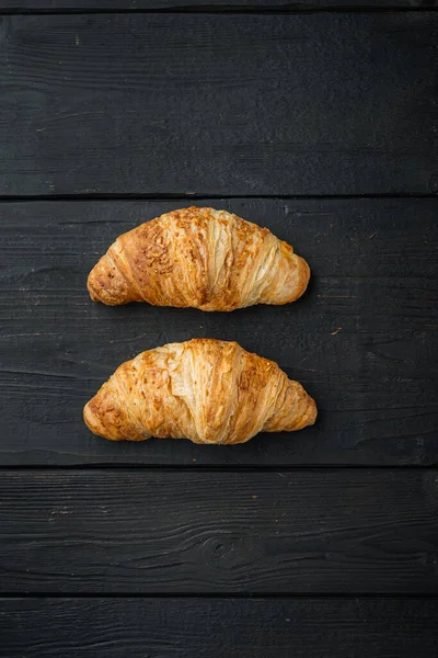 Taze pişmiş kruvasan seti, siyah ahşap masa zemininde, üst manzara düz.
