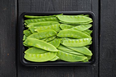 Şekerli bezelyeler, taze olgun bebek kabukları, plastik kabın içinde, siyah ahşap arka planda, üst manzara düz