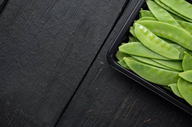 Sağlıklı bezelye seti, plastik kabın içinde, siyah ahşap zemin üzerinde, üst görünüm düz, metin için telif alanı ve boşluk ile