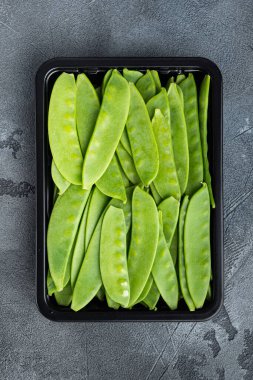 Şekerli bezelyeler, taze olgun bebek kabukları, plastik kabın içinde, gri taş arka planda, üst manzara düz.