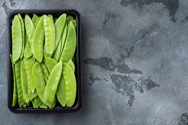 Sağlıklı bezelye seti, plastik kabın içinde, gri taş zemin üzerinde, üst görünüm düz yerde, metin için telif alanı ve boşluk ile