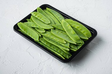 Organik Yeşil Şekerli Bezelyeler hazır, plastik kabın içinde, beyaz taş zemin üzerinde.