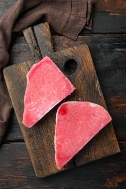 Donmuş ton balığı bifteği seti, ahşap kesim tahtasının üzerinde, eski siyah tahta masa zemininde, üst manzara düz yatıyordu.