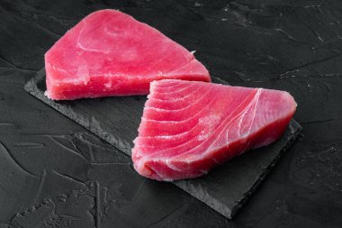 Çiğ ton balığı bifteği, taze kırmızı ton balığı fileto seti, taş tahtada, siyah taş zemin üzerinde.