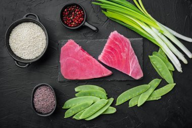 Çiğ ton balığının malzemeleri yeşil bezelye, susam ve bitkiler, taş tahtada, siyah taş zemin üzerinde, üst görünüm düz