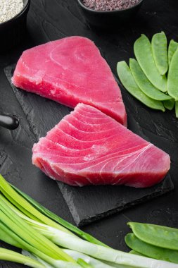 Taze çiğ ton balığı bifteği, yeşil bezelye, susam ve taze soğan seti, taş tahtada, siyah taş zemin üzerinde.