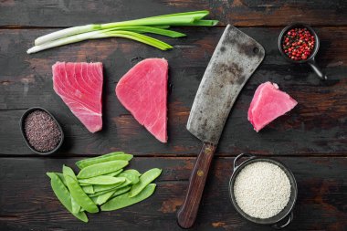 Çiğ ton balığı bifteği, taze kırmızı ton balığı fileto, yeşil bezelye, susam ve baharat seti, ve eski kasap satır bıçağı, eski ahşap masa arka planında, üst görünüm düz yatıyordu