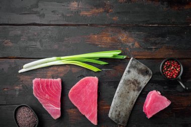 Taze taze çiğ ton balığı bifteği, yeşil bezelye, susam ve taze soğan seti, ve eski kasap satır bıçağı, eski siyah ahşap masa arka planı, üst görünüm düz, metin için yer ve mekan