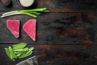 İçinde yeşil bezelye, susam ve bitkiler bulunan çiğ ton balığı parçaları, eski koyu ahşap masa arkaplanı üzerine kurulmuş, üst görünüm düz, metin alanı ve boşluğu olan